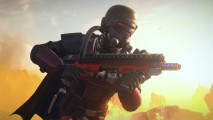 Helldivers 2 Escalation of Freedom: A soldier in an all-black armor suit with a cape holding a red and black assault rifle with flames in the background